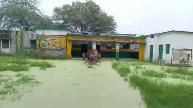 झाँसी में प्राथमिक विद्यालय में भरा हुआ पानी है बच्चो को हो रही परेशानी बच्चों को पढ़ाई करने से पहले पानी में से स्कूल।