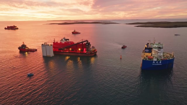 Aerial view at sunset of a red offshore vessel and a cargo ship at anchor with tugs alongside