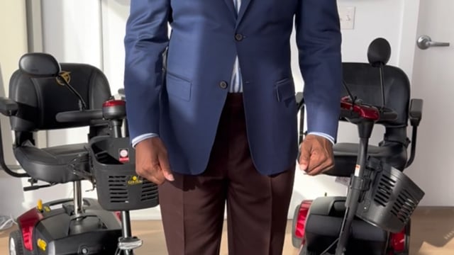 Ike, founder of Westchester Mobility Concierge, seated between 4-wheel mobility scooters with WMC branding behind him